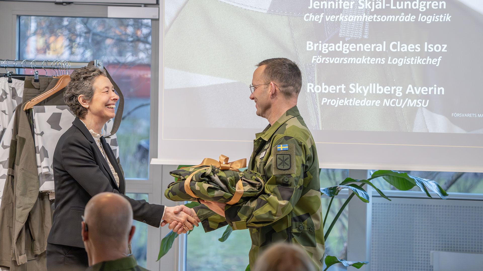 Jennifer Skjäl-Lundgren, chef för verksamhetsområde logistik på FMV överlämnar en symbolisk uniform till Försvarsmaktens logistikchef brigadgeneral Claes Isoz. 