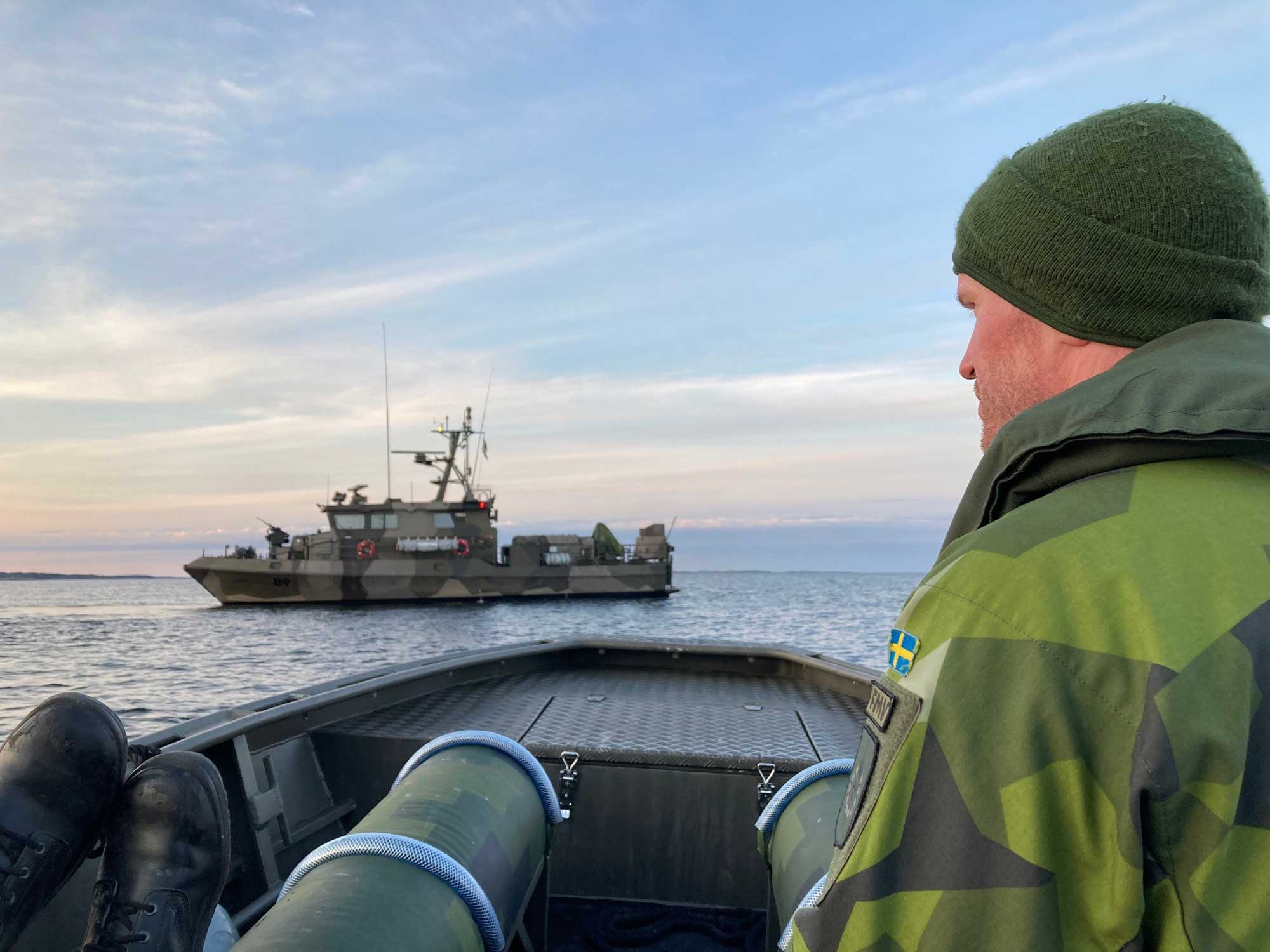 En man sitter i en båt och tittar mot en bevakningsbåt i samband med tester.