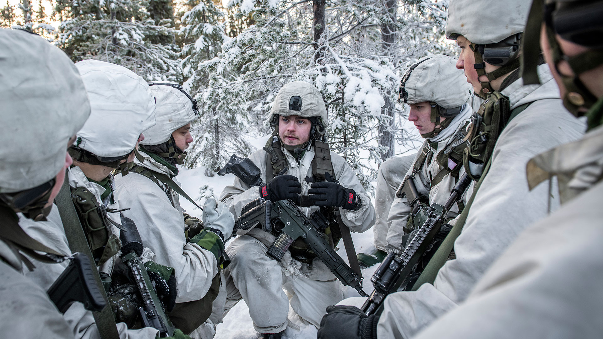 En grupp soldater i vinteruniform sitter i ring och pratar.