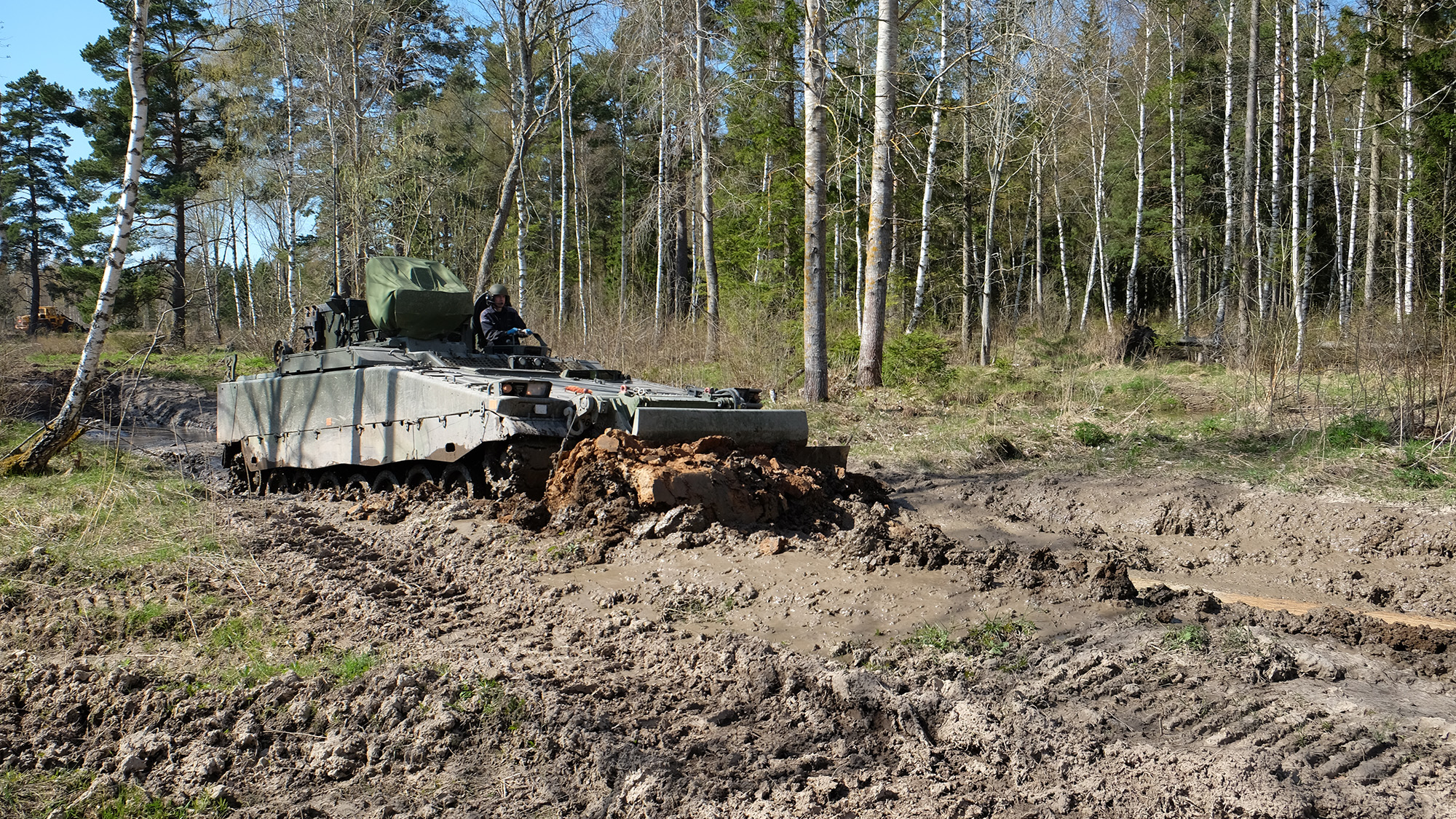 Pionjärpansarbandvagnen schaktar en stor lermassa framför sig. 