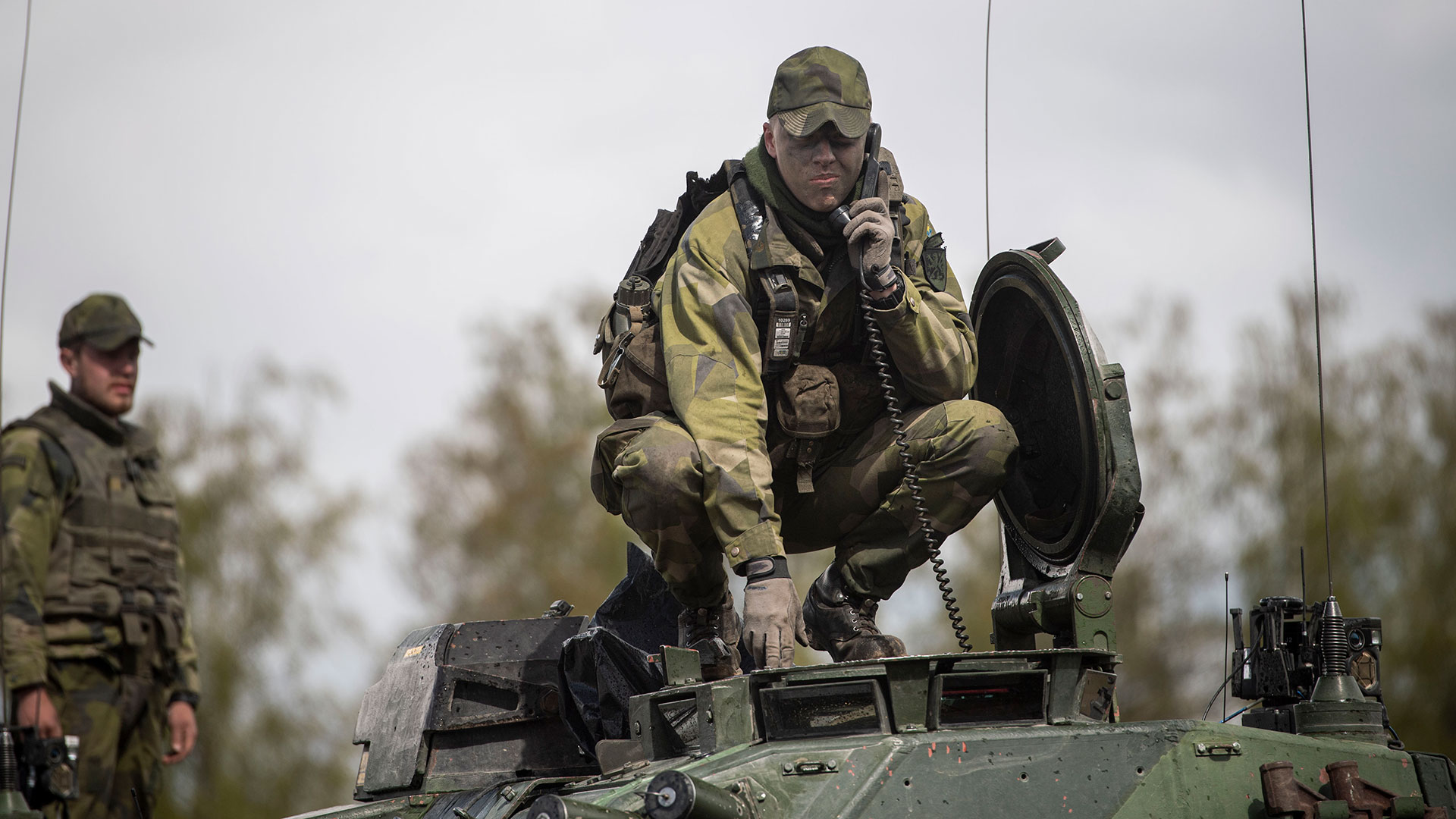 Vagnchef som står upp i en stridsvagn med huvudet utanför luckan. Han talar i en radio.