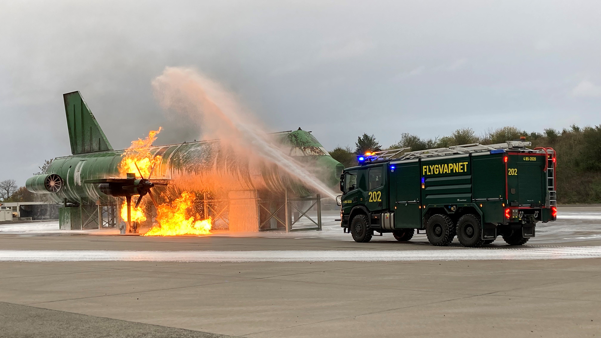 Räddningsbil sprutar släckvätska för att släcka eld i en flygplansmodell i naturlig storlek.