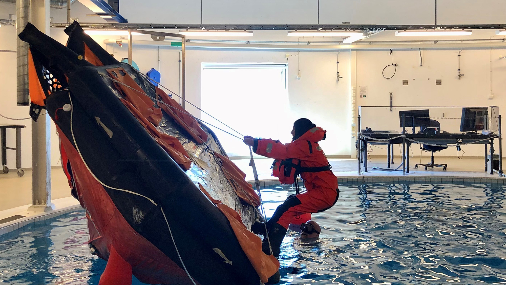 En sjöman i orange sjöräddningsväst vänder en livflotte i en bassäng. 