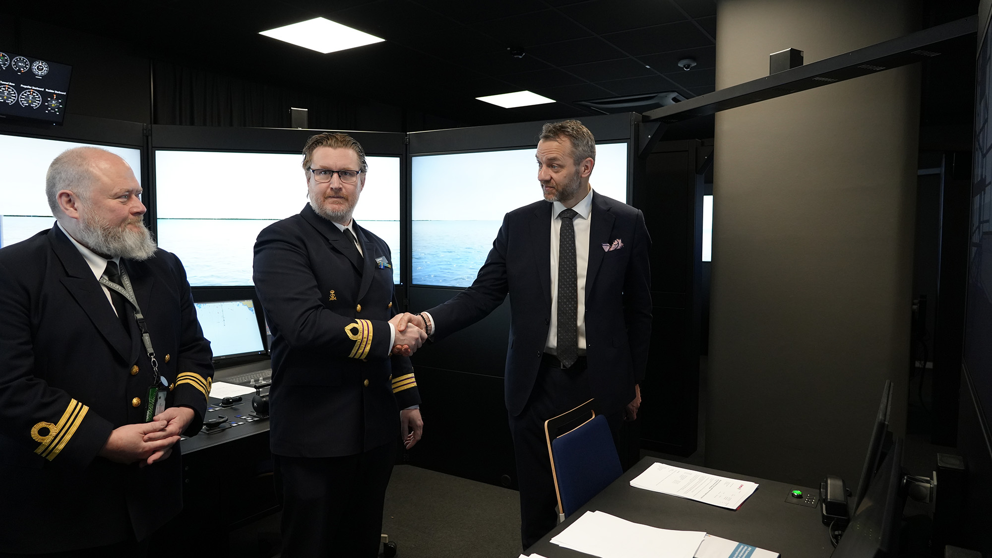 Två män tar varandra i hand och en tredje står bredvid. 