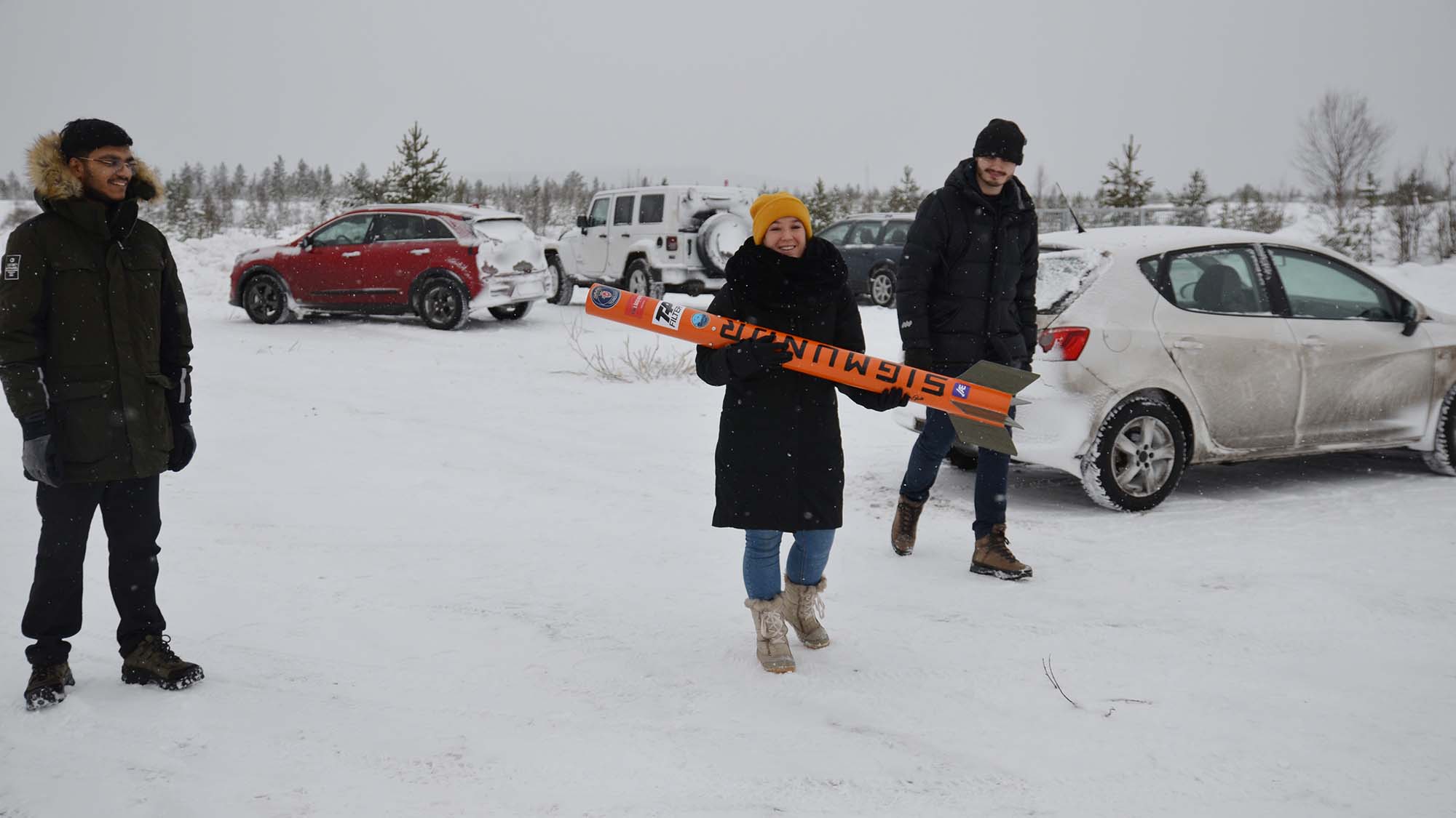 Tre personer med Sigmundr på en parkeringsplats